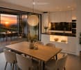 Modern kitchen and dining area with a wooden dining table, six chairs, pendant light, and a kitchen island with built-in cabinets and appliances.