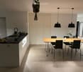 Modern kitchen with a black countertop, wooden dining table, and pendant lights. Includes a sink, faucet, and a hanging plant.