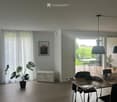 Bright dining area with tiled floor, large window with white curtains, and a view to a patio with outdoor furniture.