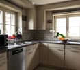 Modern kitchen with light wood cabinets, stainless steel appliances, and a black countertop. Features a double sink, microwave, and decorative items on the windowsill.