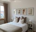 Cozy bedroom with a large bed, multiple pillows, a nightstand with a lamp, a mirror, and several framed pictures on the wall.