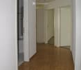 Empty hallway with wooden flooring, white walls, and several doors leading to other rooms.