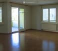 Empty room with wooden flooring, large windows, and a sliding glass door leading to a balcony.