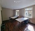 Bright room with wooden flooring, two tables, chairs, and trash bins near the wall.