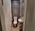 Modern bathroom with dark grey tiled walls, a toilet, a sink with a chrome faucet, and a toilet paper holder.