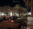 An outdoor seating area with a thatched-roof structure, featuring a sofa, chairs, a table, and potted plants, illuminated by ambient lighting.