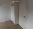 Empty room with wooden flooring, white walls, and a closed door leading to another space.
