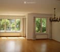 Empty room with wooden flooring, large windows with curtains, radiators, and a chandelier hanging from the ceiling.