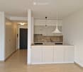 Modern kitchen with light wood cabinets, a central island, and pendant lighting. The space features a sleek design with a polished wooden floor and a visible doorway leading to another room.