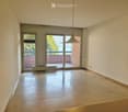 Empty room with wooden flooring, white walls, large sliding glass doors leading to a balcony, and a modern pendant light fixture.