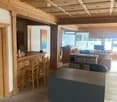 Office space with a reception desk, wooden stools, office desk, computer, and bookshelves. The ceiling features decorative wooden paneling.