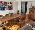 Modern living and dining area with a grey sofa, wooden dining table, leather chairs, a wooden cabinet, and a colorful abstract painting on the wall.