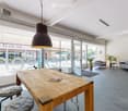 Modern, open-concept space with large windows, a wooden table, two sofas, a hanging pendant light, and potted plants.