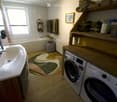 Bathroom with a sink, bathtub, washing machine, dryer, shelves with towels, and a window with blinds.