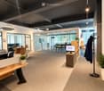 Modern office space with a reception area, desks, chairs, and a coat rack. The room features a sleek design with glass partitions and pendant lighting.