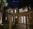 Two-story stone house with large windows and a wooden pergola, surrounded by palm trees and a stone-paved patio.