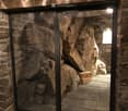 A stone-walled room with a glass display case containing large rocks, and two boxes placed on a stone platform.