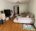 Modern living room with a sectional sofa, coffee table, TV stand, bookshelf, and a small round table. The room features wooden flooring and white walls.