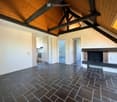 Loft-style room with exposed wooden beams, dark tiled floor, fireplace, radiator, and open kitchen area visible in the background.