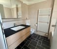 Modern bathroom with black tiled floor, wooden vanity with sink and faucet, large mirror, toilet, and white radiator.