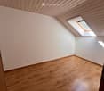 Empty room with wooden flooring, white walls, and a skylight window letting in natural light.