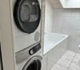 Modern bathroom with white tiled walls and floor, featuring a washing machine and a bathtub.