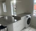 Bright, modern kitchen with white cabinets, granite countertops, a washing machine, and a black chair.