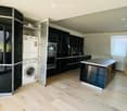 Modern kitchen with light wooden flooring, black cabinets, a central island, and a stacked washer/dryer unit.