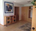 A modern, well-lit room with wooden flooring, a wooden cabinet, a chair, and a colorful picture frame on the wall.