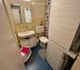 Modern bathroom with blue tiles, white fixtures, a bathtub with a pink towel, a toilet, a sink, a mirror, and a towel rack.