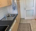 Modern kitchen with light wooden cabinets, stainless steel sink, black countertop, and decorative black and white patterned rug.