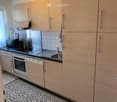 Modern kitchen with light wood cabinets, stainless steel appliances, and a black countertop. Features an oven, dishwasher, microwave, and a sink with a faucet.