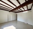 Empty room with white walls, exposed wooden ceiling beams, and tiled floor. No furniture or equipment visible.