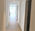 Modern hallway with light wooden flooring, white walls, recessed lighting, and open doorways leading to other rooms.