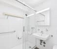 Modern bathroom with white tiles, a glass-enclosed shower, a sink with a mirror, and handrails for accessibility.