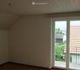 Empty room with wooden flooring, white walls, and large sliding glass doors leading to a balcony with a view of neighboring houses and greenery.