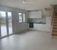 Modern kitchen with white cabinets, a sink, and an oven. Large windows and a sliding glass door lead to a balcony.