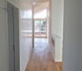 Bright, modern hallway with wooden flooring, white walls, built-in closet, and a view to a balcony area through large glass doors.