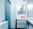 small bathroom with blue glass door, white sink, mirror, white walls, grey vanity, glass windows, radiator