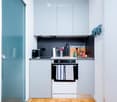 compact kitchen, electric stove, built-in dishwasher, refrigerator, coffee machine, hanging towel, white cabinets, gray countertops