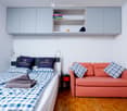 A room with twin beds, an orange couch, nightstand, and built-in cabinets.