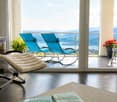 Balcony with lounge chairs, a small table, and a flower pot, offering a scenic view of a lake and mountains.