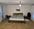 Modern bedroom with wooden flooring, a large bed with grey bedding, nightstands, a picture frame on the wall, and a white wardrobe.