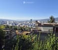 A modern building with a flat roof and a panoramic cityscape view in the background, surrounded by greenery.