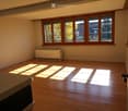 Empty room with wooden flooring, large windows with wooden frames, radiator, and natural light streaming in.