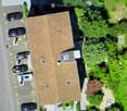 Aerial view of a two-story house with a brown roof, surrounded by greenery and parked cars.