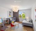 Brightly lit children's room with a grey sofa, small table, red chair, bookshelf, crib, and artwork featuring Mickey Mouse.