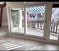 View of a tiled indoor space with large sliding glass doors leading to a covered outdoor balcony area with wooden railings.