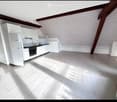 Bright, modern kitchen with white cabinets, stainless steel appliances, and tiled flooring. The space features a refrigerator, oven, and sink, with natural light streaming in from the slanted ceiling.