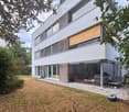 Modern two-story house with white facade, large windows, and a covered outdoor patio area. The house features a sleek design with wooden accents and a well-maintained garden.